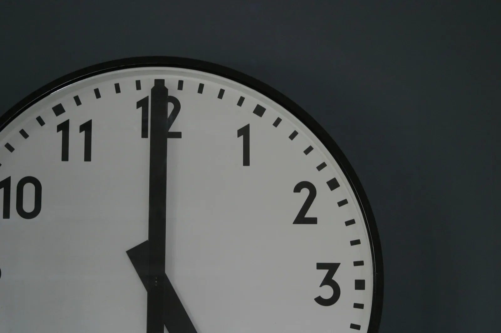 Close-up of a black-and-white wall clock reading five o’clock against a dark wall
