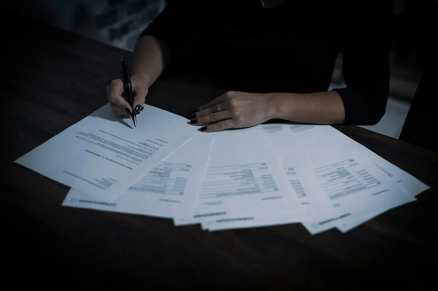 Hands reviewing a spread of printed documents on a dark table