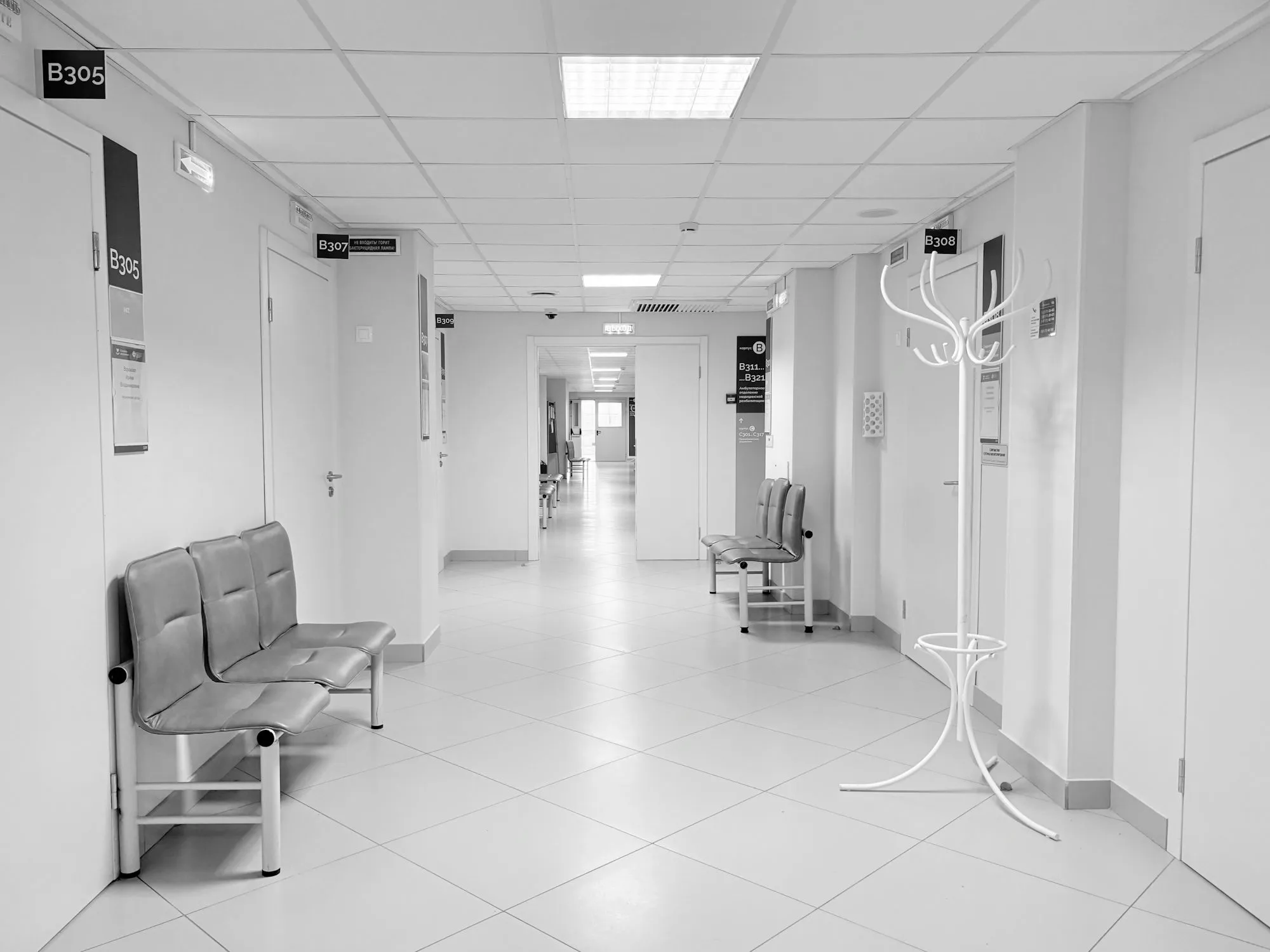 An empty clinic corridor with waiting chairs outside closed consultation rooms