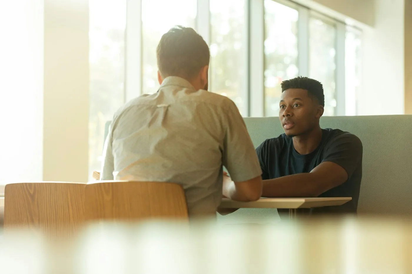 Two people in a one-on-one conversation at a table by a window