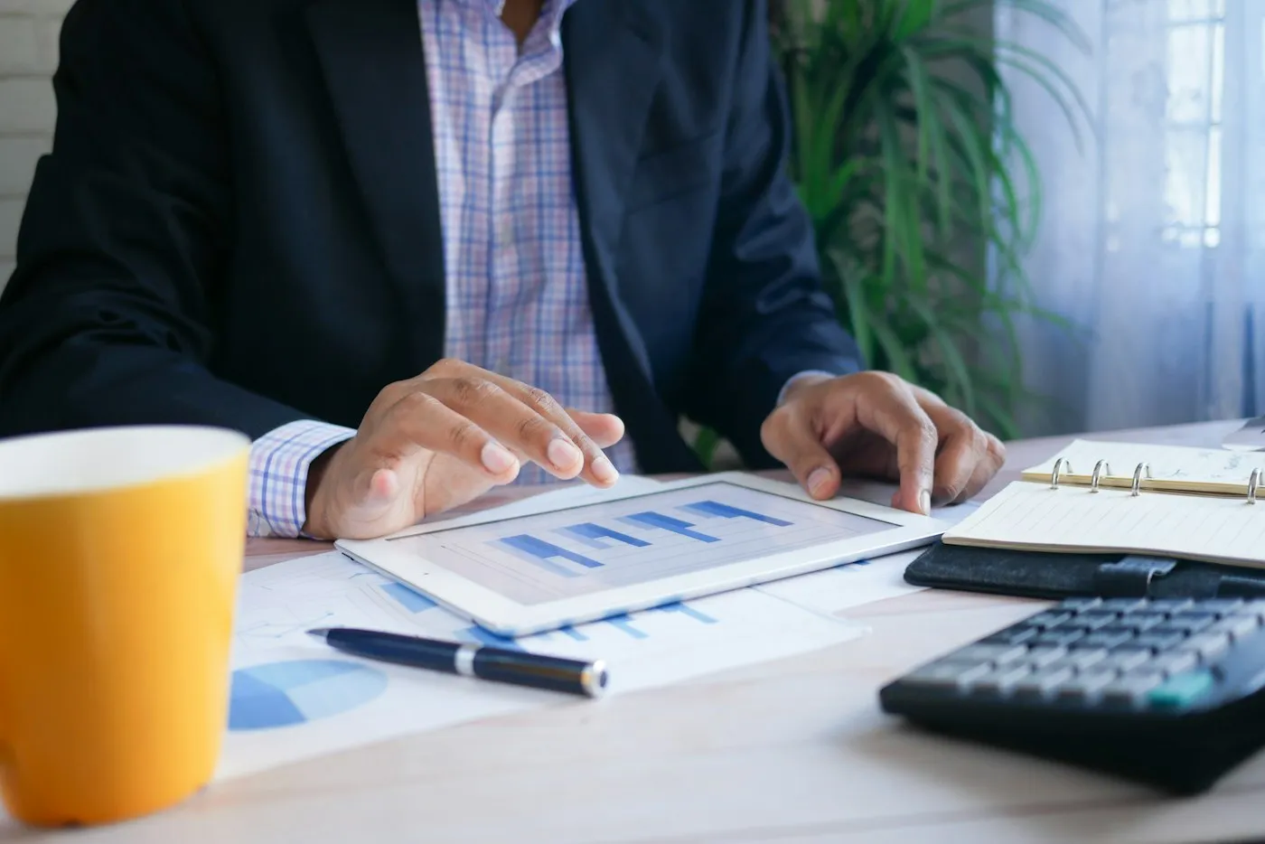 An analyst reviewing charts on a tablet beside printed reports and a calculator
